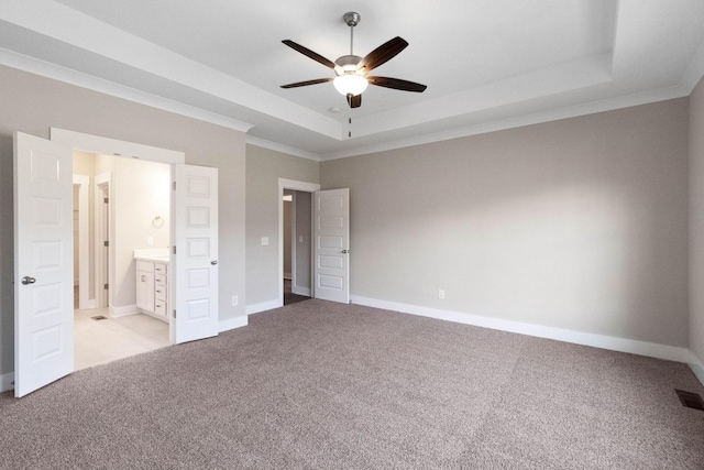 unfurnished bedroom with ceiling fan, connected bathroom, a tray ceiling, ornamental molding, and light carpet