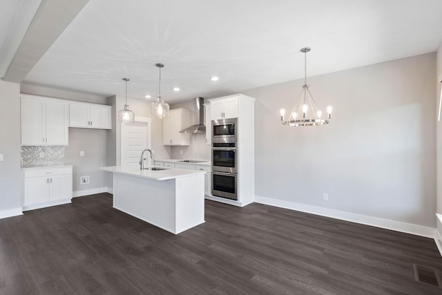 kitchen featuring white cabinetry, an island with sink, sink, stainless steel appliances, and wall chimney exhaust hood