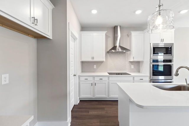 kitchen featuring wall chimney range hood, decorative light fixtures, white cabinets, and appliances with stainless steel finishes