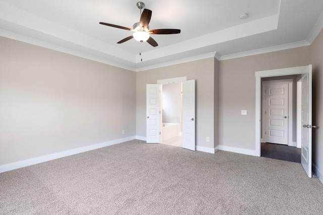 unfurnished bedroom with ensuite bath, ornamental molding, a tray ceiling, ceiling fan, and carpet