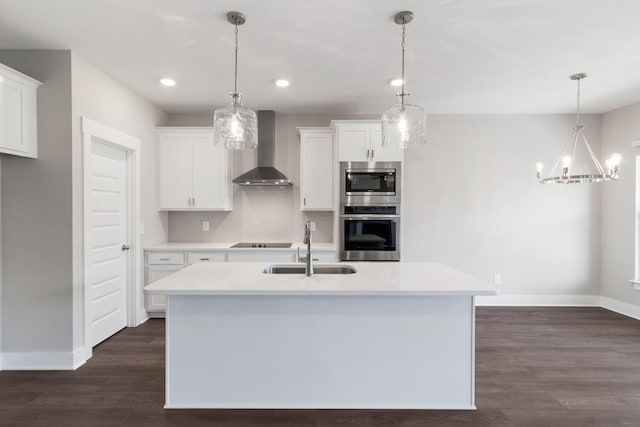 kitchen featuring wall chimney range hood, sink, white cabinetry, stainless steel appliances, and decorative light fixtures