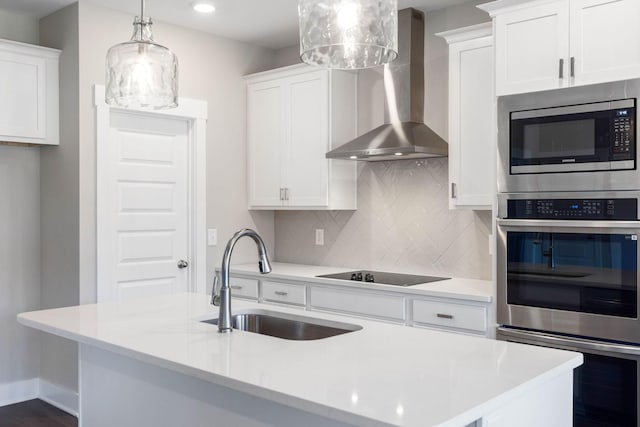 kitchen with wall chimney range hood, sink, white cabinetry, stainless steel appliances, and decorative light fixtures