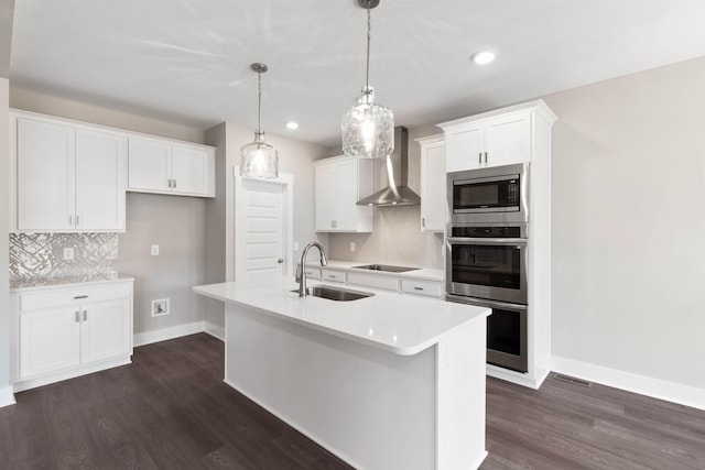 kitchen with stainless steel appliances, white cabinetry, a kitchen island with sink, and wall chimney range hood