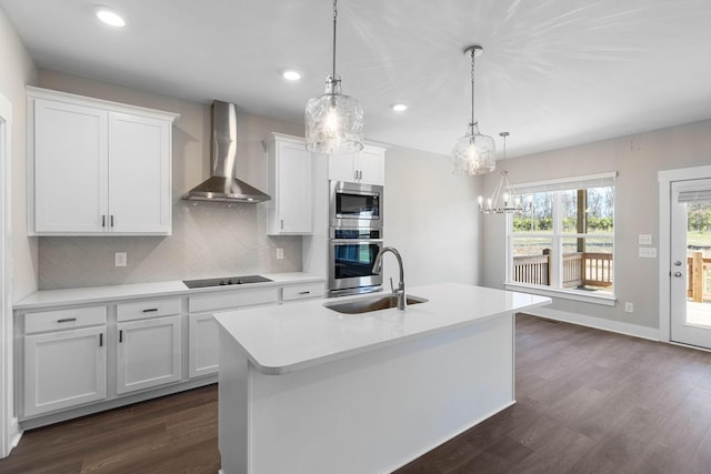 kitchen with white cabinetry, decorative light fixtures, a center island with sink, and wall chimney range hood