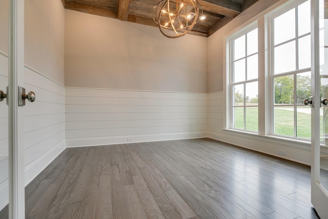 unfurnished room featuring wood-type flooring, a notable chandelier, and beam ceiling