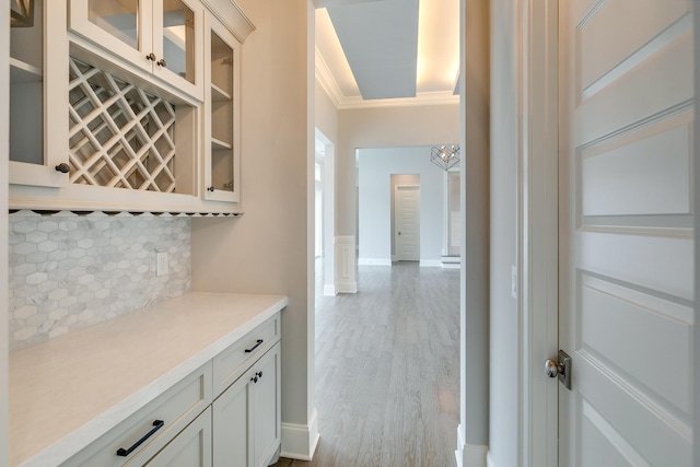 bar with white cabinetry, light hardwood / wood-style floors, crown molding, and decorative backsplash