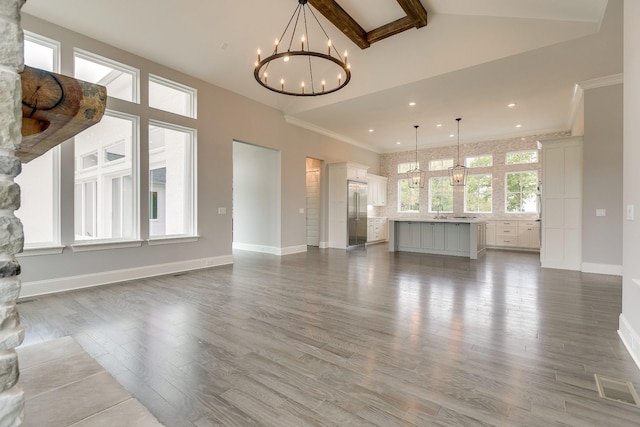 unfurnished living room with hardwood / wood-style floors, high vaulted ceiling, sink, a chandelier, and crown molding