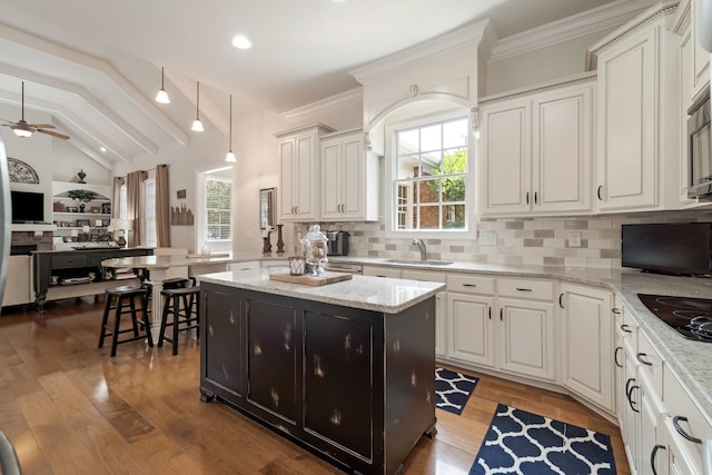 kitchen with a center island, sink, light stone counters, and decorative light fixtures