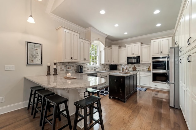 kitchen featuring appliances with stainless steel finishes, tasteful backsplash, hanging light fixtures, hardwood / wood-style flooring, and kitchen peninsula