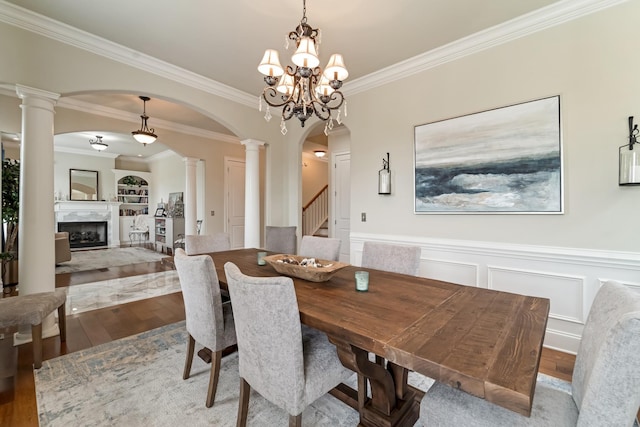 dining space featuring a premium fireplace, an inviting chandelier, decorative columns, wood-type flooring, and ornamental molding