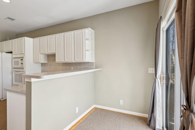 kitchen featuring white cabinetry, tasteful backsplash, light colored carpet, kitchen peninsula, and white appliances