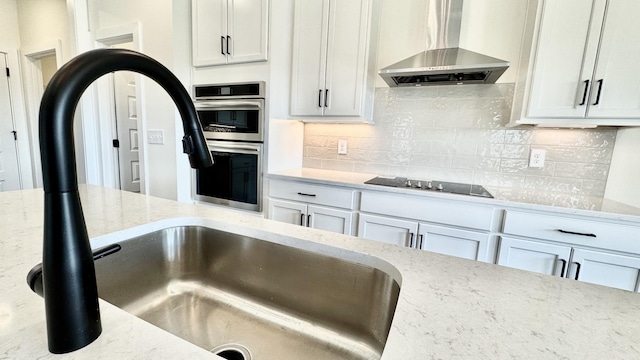 kitchen with sink, wall chimney exhaust hood, light stone counters, black electric stovetop, and stainless steel double oven