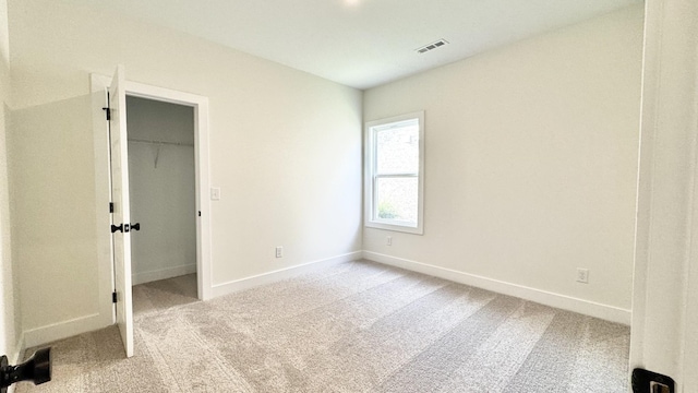 unfurnished bedroom with a walk in closet, light colored carpet, and a closet