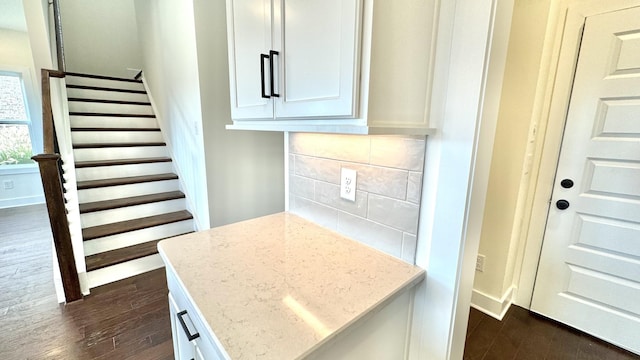 interior space featuring dark wood-type flooring, backsplash, white cabinets, and light stone counters