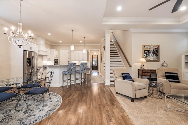 living room featuring a raised ceiling, ornamental molding, ceiling fan with notable chandelier, and hardwood / wood-style floors