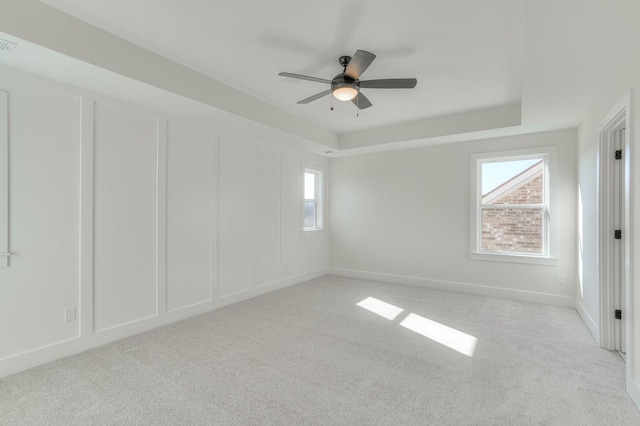 empty room with ceiling fan, light colored carpet, and a tray ceiling