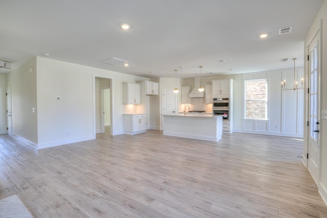 unfurnished living room featuring a notable chandelier, light hardwood / wood-style floors, and sink