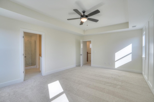 spare room featuring ceiling fan, light colored carpet, and a raised ceiling