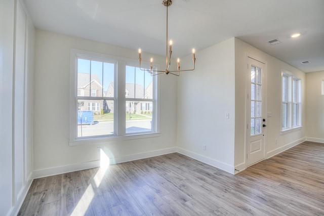 unfurnished dining area featuring an inviting chandelier and light hardwood / wood-style flooring