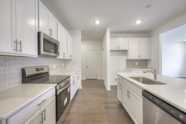 kitchen featuring sink, white cabinetry, wood-type flooring, stainless steel appliances, and backsplash