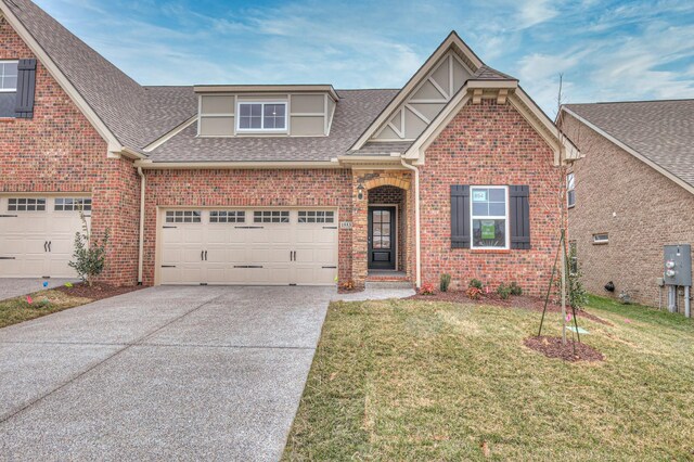 view of front of home featuring driveway, a shingled roof, a front lawn, a garage, and brick siding