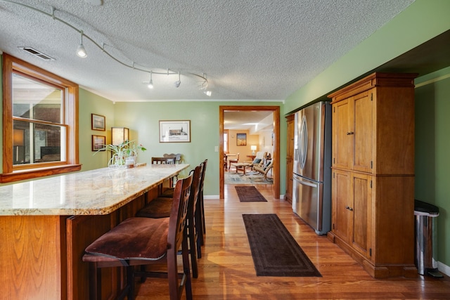 kitchen with hardwood / wood-style floors, a kitchen breakfast bar, light stone countertops, a textured ceiling, and stainless steel fridge with ice dispenser