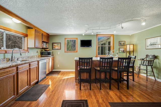 kitchen featuring appliances with stainless steel finishes, sink, a breakfast bar area, light stone countertops, and light wood-type flooring