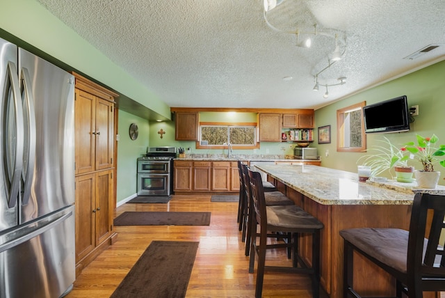 kitchen with appliances with stainless steel finishes, a kitchen breakfast bar, light stone counters, light hardwood / wood-style floors, and a textured ceiling