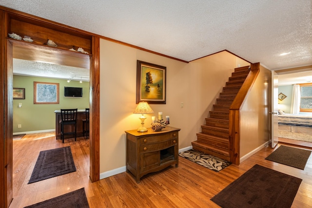 staircase with ornamental molding, wood-type flooring, and a textured ceiling