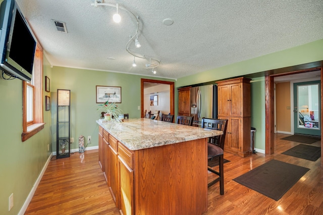 kitchen featuring a kitchen breakfast bar, a center island, stainless steel refrigerator with ice dispenser, light stone counters, and light wood-type flooring