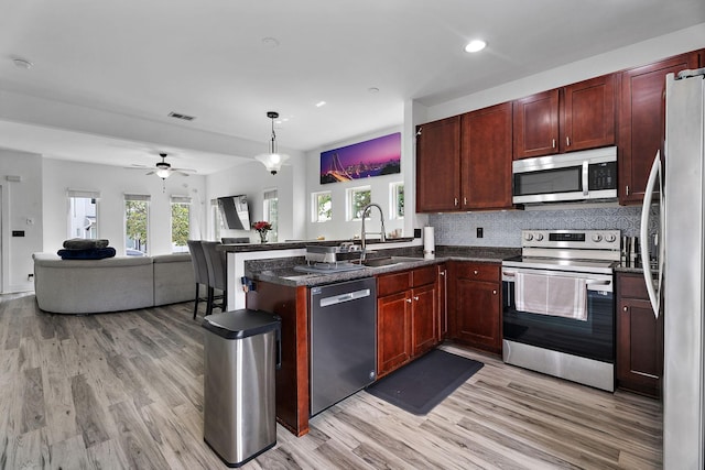 kitchen with pendant lighting, sink, light hardwood / wood-style flooring, backsplash, and stainless steel appliances