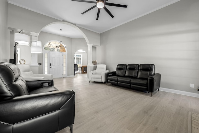 living area featuring light wood-style floors, arched walkways, crown molding, and decorative columns