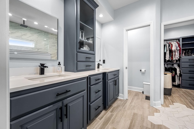 full bathroom featuring double vanity, tiled shower, a sink, and wood tiled floor