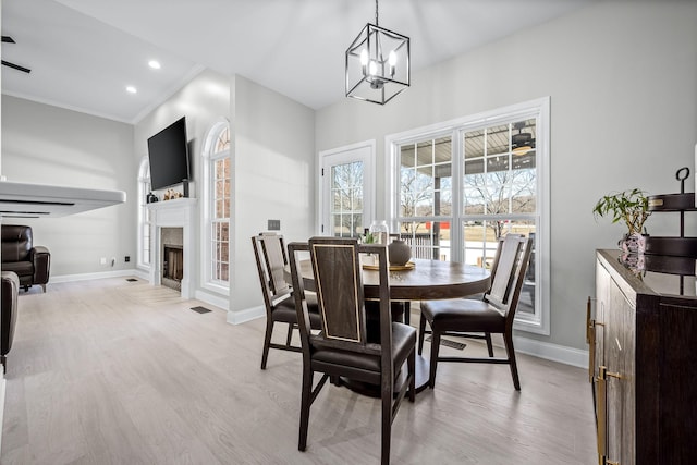 dining space with crown molding, light wood finished floors, a fireplace with flush hearth, and baseboards