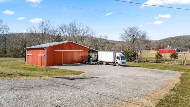 view of pole building with gravel driveway, a yard, and a wooded view