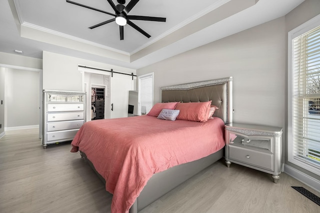 bedroom with a barn door, crown molding, a tray ceiling, and wood finished floors