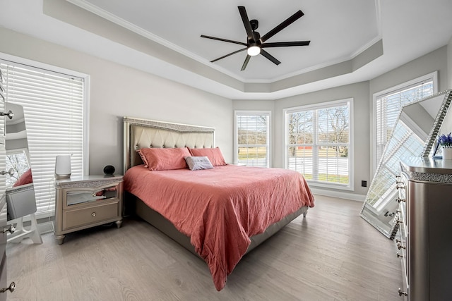 bedroom with ceiling fan, ornamental molding, light wood-type flooring, and a raised ceiling