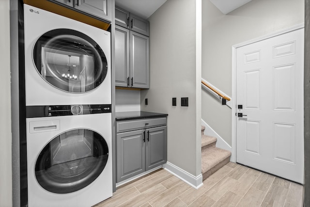 clothes washing area featuring stacked washer / dryer, cabinet space, baseboards, and wood finish floors