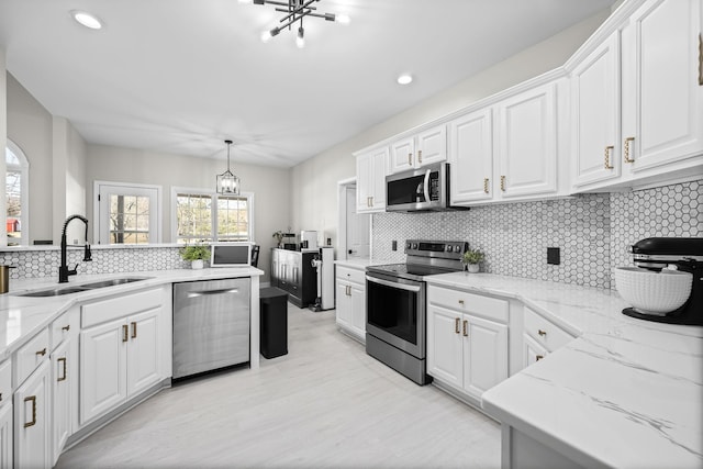 kitchen featuring stainless steel appliances, an inviting chandelier, white cabinets, a sink, and light stone countertops