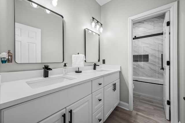 full bathroom with double vanity, shower / bath combination with glass door, a sink, and wood finished floors