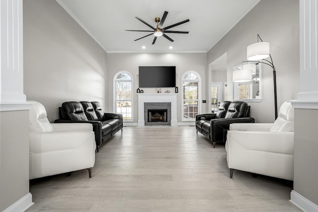 living area featuring crown molding, light wood-style flooring, a tiled fireplace, and ceiling fan