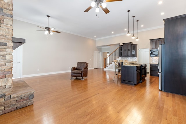 kitchen featuring an island with sink, open floor plan, hanging light fixtures, built in microwave, and light countertops