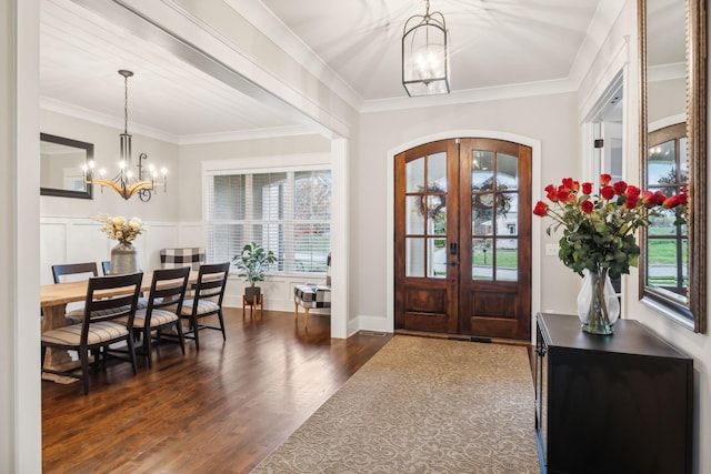 entrance foyer featuring an inviting chandelier, dark wood-type flooring, ornamental molding, and french doors