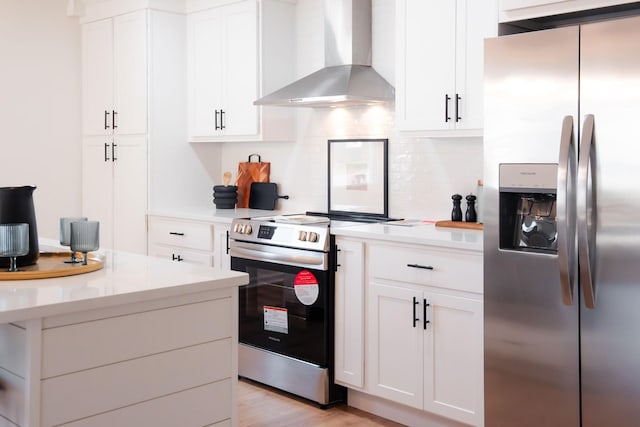 kitchen with wall chimney range hood, stainless steel appliances, light hardwood / wood-style floors, white cabinets, and decorative backsplash