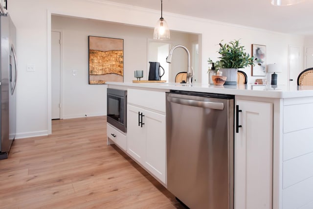 kitchen with stainless steel appliances, ornamental molding, light hardwood / wood-style floors, white cabinets, and decorative light fixtures