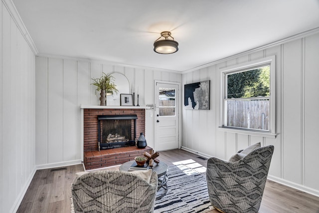 living area featuring ornamental molding, hardwood / wood-style floors, and a brick fireplace