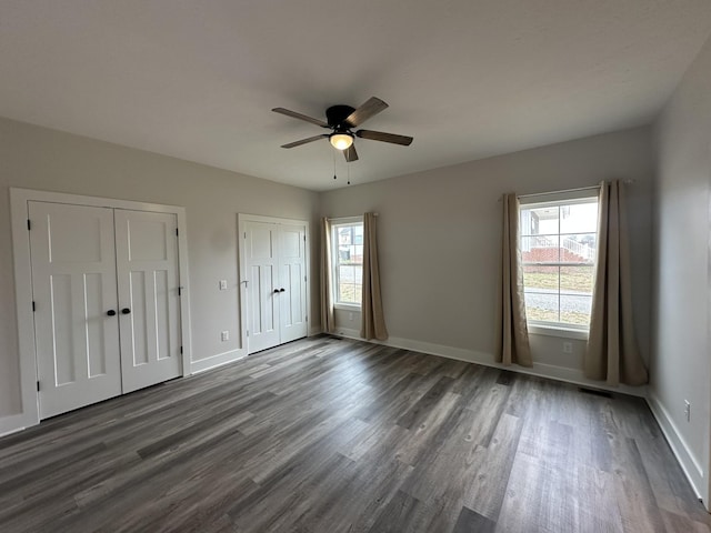 unfurnished bedroom with dark wood-style floors, a ceiling fan, baseboards, and multiple closets