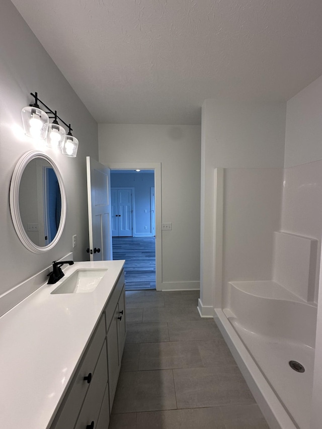 full bathroom with a shower, vanity, a textured ceiling, baseboards, and tile patterned floors