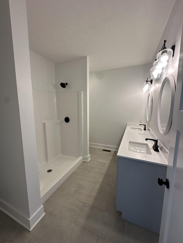 bathroom with a textured ceiling, baseboards, walk in shower, and a sink