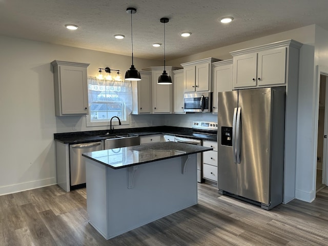 kitchen with appliances with stainless steel finishes, dark wood finished floors, a center island, and a sink